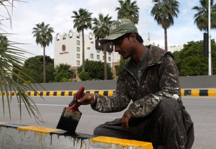 عامل يدهن الأرصفة استعدادًا لزيارة وفدين أمريكي وإيراني إلى إسلام آباد